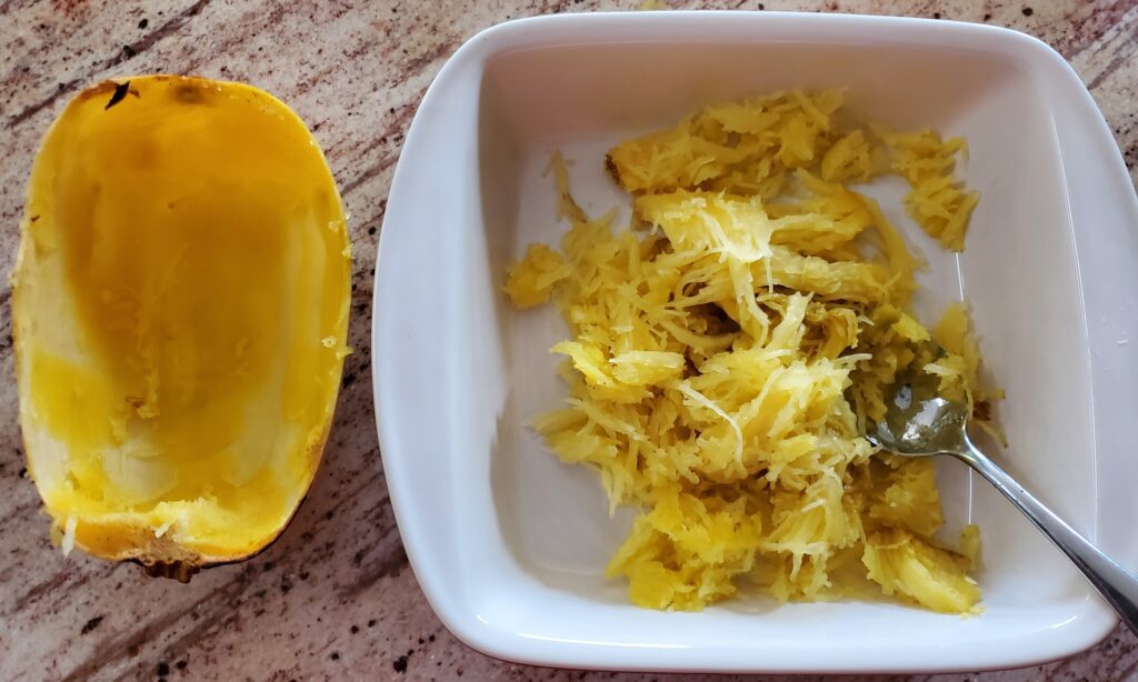 Scooping spaghetti squash into a baking dish